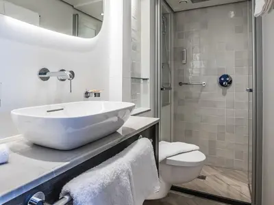Modernes und helles Badezimmer an Bord der MS Annabelle. Zu sehen sind ein weißer Waschtisch, eine Duschkabine mit Haltegriff und eine Toilette. Die Einrichtung ist minimalistisch gehalten.