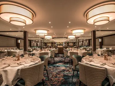 Das stilvolle Restaurant der MS Annabelle zeigt elegant gedeckte Tische, einzigartige Deckenleuchten und einen gemusterten Teppich. Weinregale im Hintergrund.