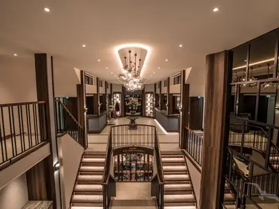 Die elegante Atrium-Lobby der MS Annabelle mit geschwungener, beleuchteter Treppe. Ein moderner Kronleuchter hängt oben. Seitliche Galerien und Shops sind erkennbar. Warme Holzakzente.