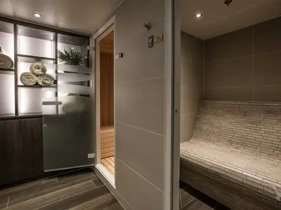 Ein moderner Spa-Bereich an Bord der MS Annabelle. Zu sehen sind ein Saunazugang mit Glastür und eine geflieste Dampfbadbank. Rolltücher und Pflanzen dekorieren den Bereich.