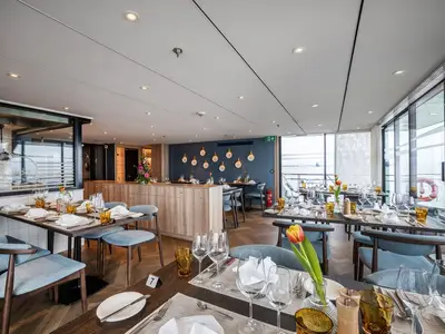 Ein modernes Restaurant an Bord der MS Annika mit gedeckten Tischen und blauen Stühlen. Große Fensterfronten bieten einen weiten Blick auf das Wasser.