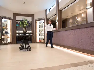 Eine freundliche Crew-Mitarbeiterin geht an der modernen Rezeption und einem Shopbereich der MS Annika vorbei. Auslagen mit Handtaschen und Schmuck sind zu sehen.