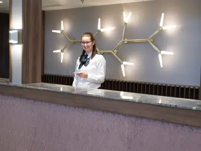 Eine freundliche Crew-Mitarbeiterin lächelt an der Rezeption der MS Annika. Sie trägt Uniform und hält eine Karte. Im Hintergrund moderne Beleuchtung und Fächer.