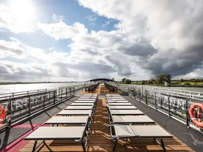 Blick auf das leere Sonnendeck der MS Annika mit zahlreichen Liegestühlen und Tischen unter einem Sonnendach auf einem Fluss. Am Rand sind die Buchstaben 'ANNIKA' zu sehen.
