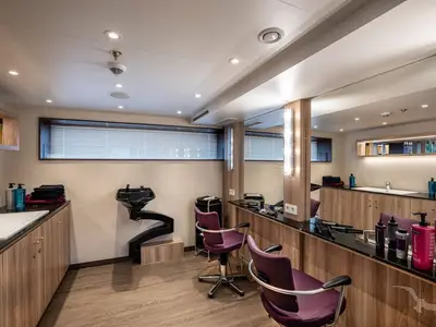Moderner Friseursalon an Bord der MS Annika mit Frisierplätzen, Spiegeln, violetten Stühlen und Haarwaschbecken. Helle Holzeinrichtung und viele Produkte sind zu sehen.