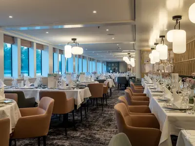 Ein geräumiges, elegantes Restaurant an Bord der MS Antonia. Tische sind weiß gedeckt mit Geschirr und Gläsern, bereit für Gäste. Große Fenster bieten Blick auf eine Wasserlandschaft. Die Beleuchtung ist modern und warm.