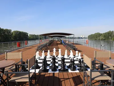 Das Sonnendeck der MS Antonia mit großem Schachspiel, Liegestühlen und Tischen. Im Hintergrund Fluss, bewaldete Ufer und Kühltürme.