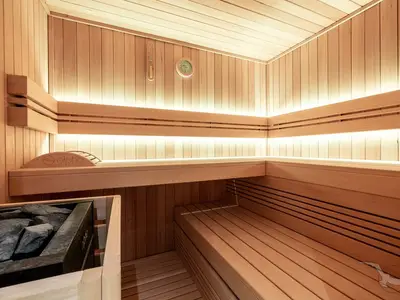 Eine moderne Sauna aus hellem Holz mit breiten Sitzbänken und indirekter Beleuchtung an Bord der MS Antonia. An der Wand hängen ein Thermometer und ein Hygrometer.
