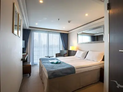 Heller Blick in eine modern eingerichtete Balkonkabine an Bord der MS Ariana mit Doppelbett, Sitzbereich und großen Fenstern, die Tageslicht hereinlassen.
