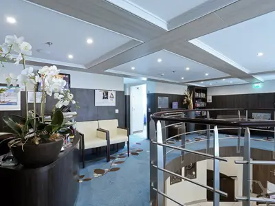 Innenansicht der Lounge und Bibliothek an Bord der MS Ariana. Mit Orchideen, bequemen Sesseln und einem Bücherregal. Ein eleganter Treppenaufgang ist im Bild. Modernes Ambiente.