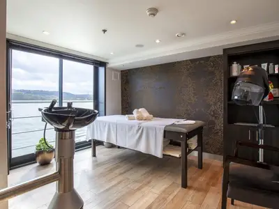 Modernes Spa an Bord der MS Ariana mit Massagebank, Haarwaschbecken und Trockenhaube. Große Fenster bieten weiten Blick auf die Flusslandschaft.