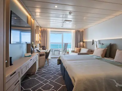 Die helle Balkonkabine an Bord der MS Artania bietet ein Doppelbett, eine Sitzecke, einen Schreibtisch und einen Balkon mit Meerblick. Die Einrichtung ist modern und in hellen Tönen gehalten.