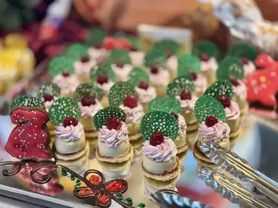 Desserts an Bord der MS Artania: Nahaufnahme von Törtchen mit pinker Creme, Himbeeren und grünen Dekorationen. Ein roter Keks und eine Zange auf dem Buffet.
