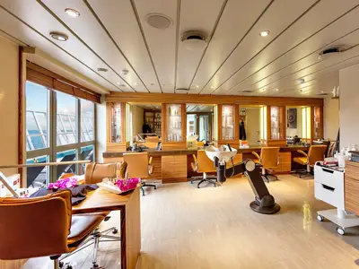 Ein heller Beauty-Salon an Bord der MS Artania mit großen Fenstern zum Meer. Mehrere Friseurstühle, Spiegel und ein Waschbecken sind sichtbar. Ohne Personen.