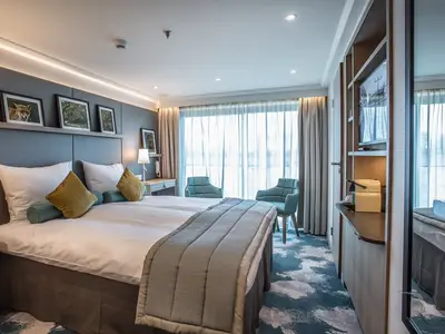 Eine helle, moderne Außenkabine an Bord der MS Asara mit einem gemütlichen Doppelbett, zwei blauen Sesseln und großem Fenster. Rechts eine TV-Einheit mit Kaffeemaschine.