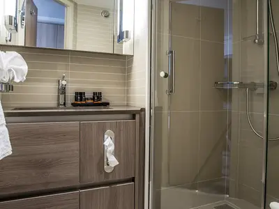 Das Badezimmer einer Kabine an Bord der MS Asara: Waschtisch, Spiegel, helle Fliesen, moderne Glasduschkabine. Toilettenartikel und frische Handtücher sind zu sehen.