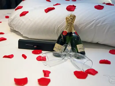 Nahaufnahme von zwei Moët & Chandon Champagnerflaschen mit Gläsern und roten Rosenblättern auf einem weißen Bett an Bord der MS Asara. Eine schwarze Geschenkbox liegt daneben.