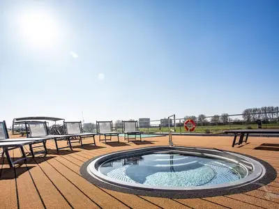 Blick auf den runden Whirlpool und mehrere leere Sonnenliegen auf dem Holzdeck der MS Asara. Im Hintergrund sind Bäume und Gebäude unter klarem, blauem Himmel zu sehen.