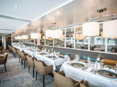 Elegantes, helles Restaurant an Bord der MS Asara. Zahlreiche Tische mit weißen Tischdecken, Geschirr und Blumen. Moderne Deckenleuchten und gemütliche Sitzbereiche füllen den Raum.