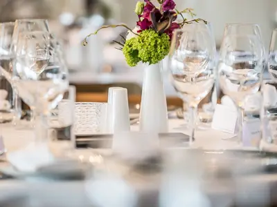 Nahaufnahme eines elegant gedeckten Tisches mit Weingläsern, Blumengesteck und Keramikvasen im Restaurant der MS Asara. Im unscharfen Hintergrund sind weitere Tische sichtbar.