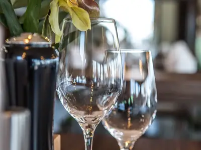 Detailaufnahme im Spezialitätenrestaurant an Bord der MS Asara: Zwei glänzende Weingläser und ein dunkler Behälter auf einem Tisch mit weichem Bokeh im Hintergrund.