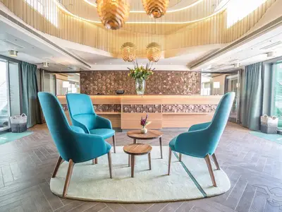 Die moderne Rezeption an Bord der MS Asara. Türkisfarbene Sessel vor einer Holztheke mit dekorativer Rückwand. Eine einladende Atmosphäre.
