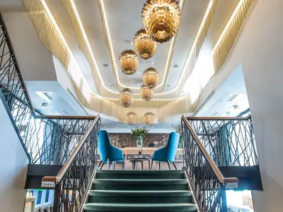 Die zentrale Treppe an Bord der MS Asara führt zu einem eleganten Empfangsbereich mit blauen Stühlen, einem Tresen und auffälligen goldenen Deckenleuchten.