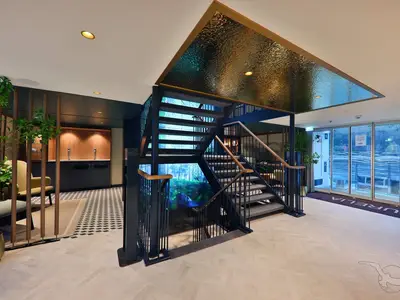 Modernes Foyer der MS Aurelia mit zentraler Treppe und digitalen Waldszenen. Links Sitzbereiche und Bar, rechts Panoramafenster zur Flusslandschaft.