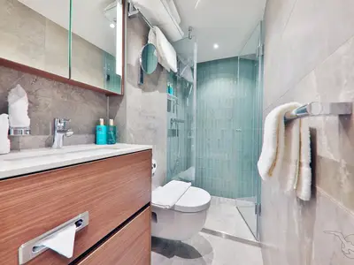 Ein modernes Badezimmer an Bord der MS Aurelia mit Waschtisch, Spiegel, verglaster Dusche mit blau-grünen Fliesen und Toilette.