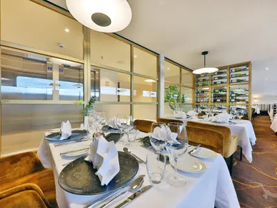 Blick ins stilvolle Restaurant an Bord der MS Aurelia. Weiße Tische sind gedeckt mit Gläsern und Besteck. Goldene Akzente und ein beleuchtetes Weinregal prägen das elegante Ambiente.
