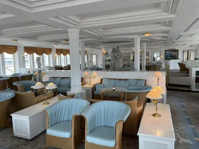 Die stilvolle Bar-Lounge der MS Deutschland ist hell und einladend mit hellblauen Polstermöbeln, Korbsesseln, dekorativen Lampen und klassischen Skulpturen. Eine helle, luxuriöse Atmosphäre auf See.