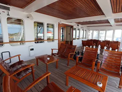 Blick auf den Außenbereich der Adlon Lounge der MS Deutschland. Edle Holzmöbel und ein Großschachspiel auf dem Teakholzdeck. Große Fensterfront mit Blick auf Hafen und Meer.