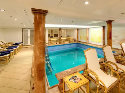 Innenpool der MS Deutschland mit hellblauem Wasser, umgeben von Liegestühlen, marmorierten Säulen und Wandbildern. Eine ruhige, klassische Spa-Atmosphäre.