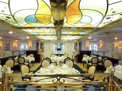 Das elegante Restaurant Vier Jahreszeiten an Bord der MS Deutschland. Gedeckte Tische und eine farbenprächtige Jugendstil-Decke bestimmen das klassische Ambiente.