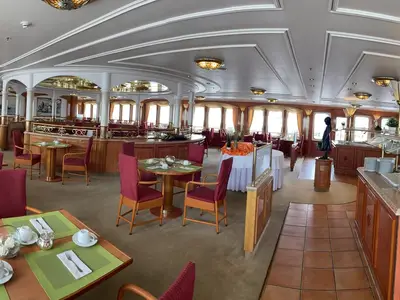 Das helle und weitläufige Lido-Restaurant an Bord der MS Deutschland mit roten Stühlen, Holztischen und einem Buffetbereich. Große Fensterfronten bieten Tageslicht.