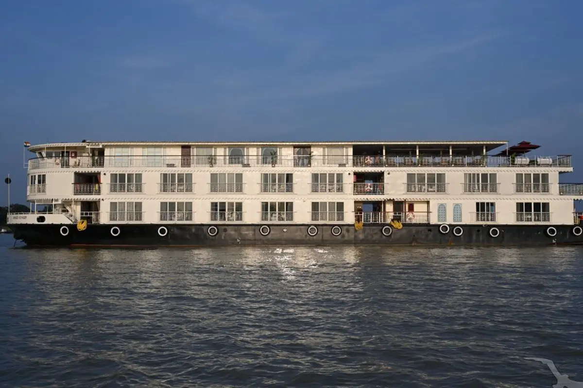 Die MS Ganges Voyager, ein weiß-schwarzes Flusskreuzfahrtschiff mit Balkonen, gleitet auf dem Wasser. Im Hintergrund ist ein klarer blauer Himmel zu sehen.