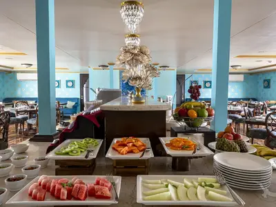Ein reichhaltiges Obstbuffet mit Kiwis, Papayas, Äpfeln und Bananen an Bord der MS Ganges Voyager. Der elegante Restaurantbereich ist in Blautönen und Gold gehalten.