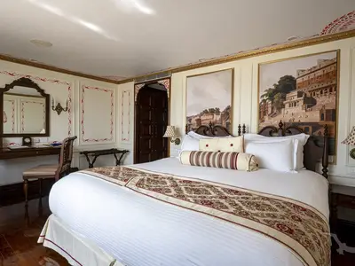 Eine elegante Suite an Bord der MS Ganges Voyager mit einem großen Bett, Schreibtischecke und zwei Wandgemälden von Flusslandschaften.