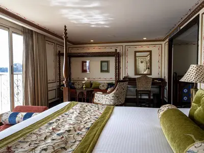 Geräumige, elegant eingerichtete Suite der MS Ganges Voyager mit Himmelbett, Sitzecke, Schreibtisch und privatem Balkon mit Flussblick.