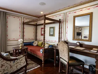 Elegante Suite an Bord der MS Ganges Voyager mit einem kunstvoll geschnitzten Himmelbett, Schreibtisch mit Stuhl und traditioneller Dekoration. Ein Spiegel reflektiert den Raum.