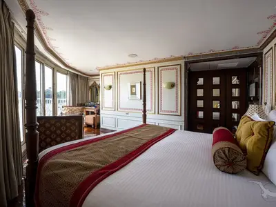 Eine opulente Suite an Bord der MS Ganges Voyager mit einem Himmelbett, reich verzierter Einrichtung und großen Fenstern mit Blick ins Grüne.