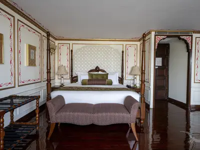 Luxuriöse Suite an Bord der MS Ganges Voyager. Großes Bett mit Zierkopfteil, grünen Kissen. Rote und goldene Wandornamente. Eleganter Sessel.