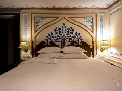 Ein elegant eingerichtetes Schlafzimmer an Bord der MS Ganges Voyager. Das weiße Bett hat ein kunstvolles blau-goldenes Kopfteil und zwei seitliche Wandlampen.
