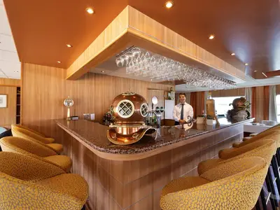 Blick in die elegante Bar-Lounge der MS Junker Jörg mit Bartresen, Hockern und einem Barkeeper. Dekoriert mit antiken Taucherhelmen.