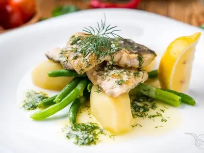 Teller mit gebratenem Fischfilet, Salzkartoffeln, grünen Bohnen und Zitrone, garniert mit Dill und Sauce. Ein frisches Gericht an Bord der MS Junker Jörg.
