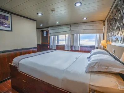 Helle Außenkabine der MS Lan Diep mit Doppelbett, weißer Bettwäsche und zwei großen Fenstern. Der Ausblick zeigt eine weite Wasserfläche unter bewölktem Himmel.