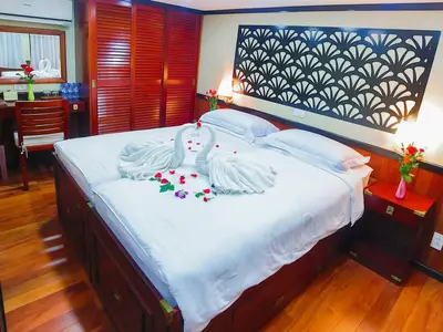 Romantisch dekorierte Außenkabine an Bord der MS Lan Diep. Doppelbett mit Handtuch-Schwänen, Rosenblättern und Holzmöbeln.