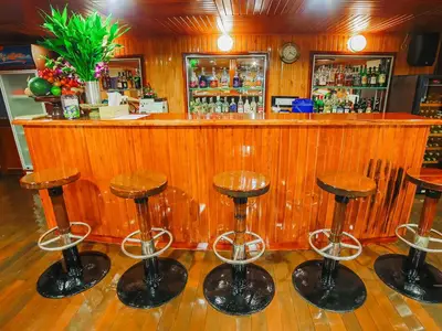Eine einladende Bar an Bord der MS Lan Diep mit warmer Holzvertäfelung, glänzenden Barhockern, einer großen Auswahl an Spirituosen und frischen Früchten als Dekoration.
