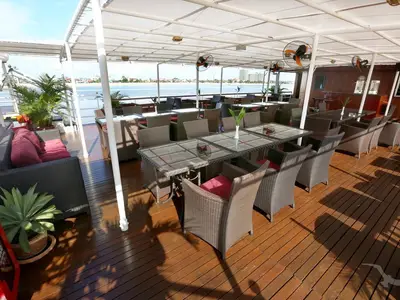 Blick auf den überdachten Restaurantbereich an Bord der MS Lan Diep mit zahlreichen Tischen, Stühlen und Sofas sowie Weitblick auf das Wasser und die Uferbebauung.