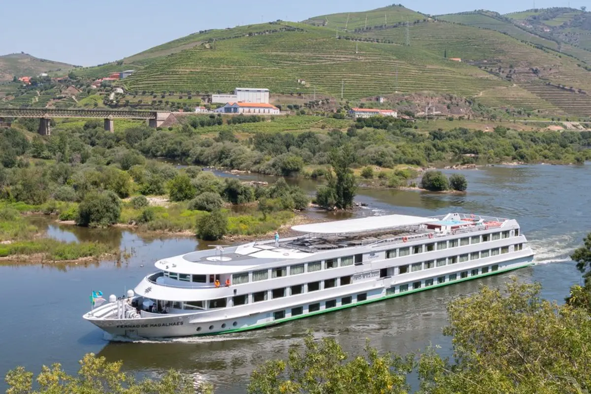 Blick von oben auf die MS Magellan, die einen Fluss entlangfährt. Im Hintergrund sind grüne, terrassierte Hügel und ein Eisenbahnviadukt zu sehen.